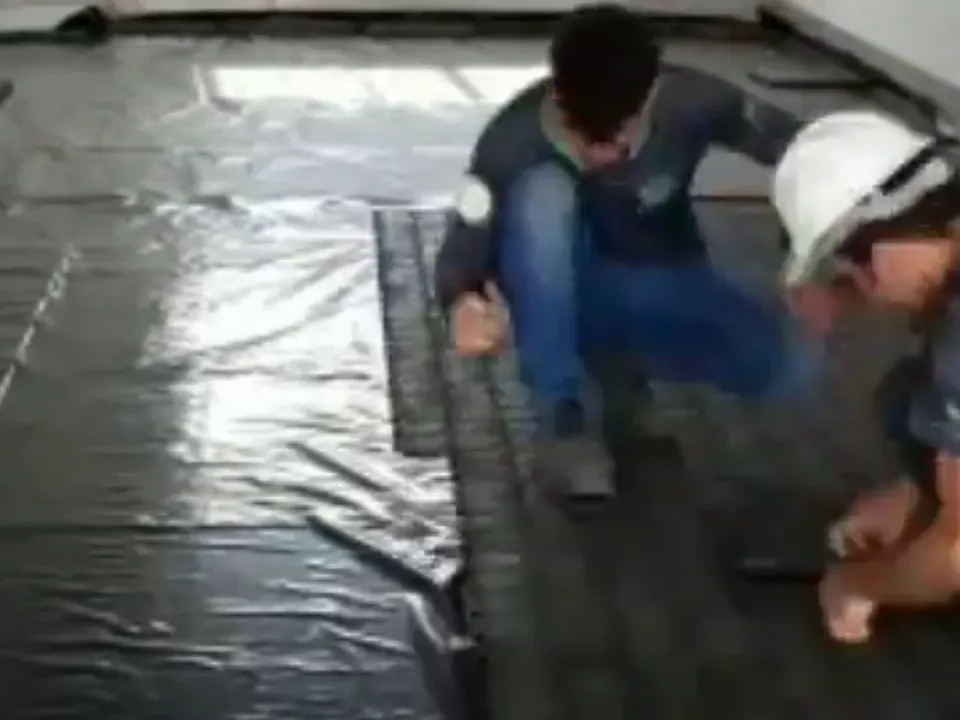 Dois instaladores encaixando placas pretas de proteção sobre uma lona estendida no piso de uma sala