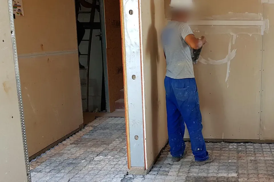 Profissional aplicando gesso na parede com o piso coberto pelas placas