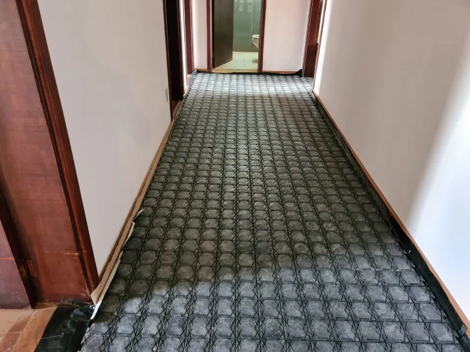 Corredor com piso de madeira coberto de parede a parede pelas placas pretas de encaixe