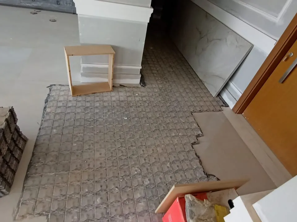 Placas de proteção sendo recolhidas de um ambiente com porcelanato claro, com parte do piso já à mostra e pilhas de placas ao lado