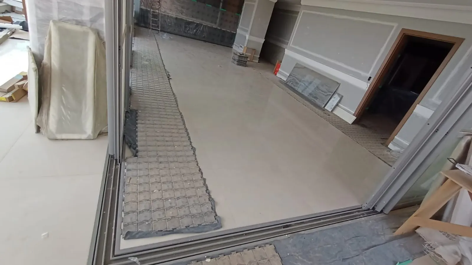 Sala com porcelanato polido de grande formato e um caminho de placas de proteção junto à esquadria da varanda